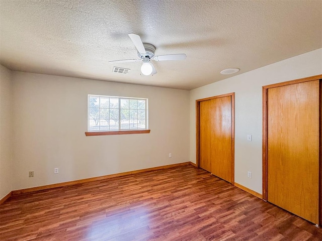 unfurnished bedroom with hardwood / wood-style floors, ceiling fan, a textured ceiling, and two closets