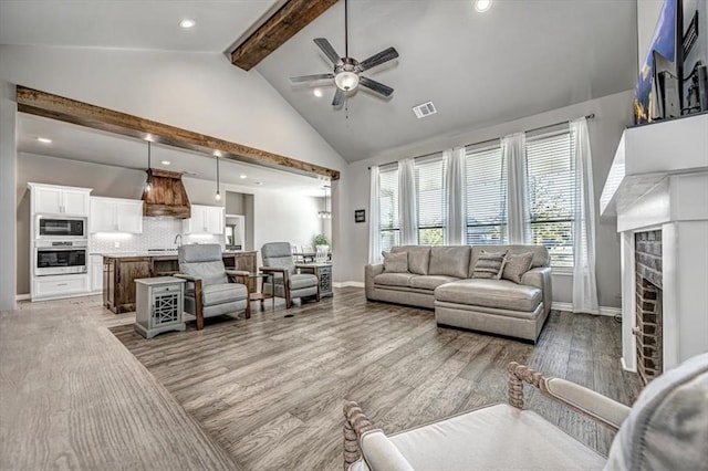 living room featuring a fireplace, ceiling fan, hardwood / wood-style flooring, high vaulted ceiling, and beamed ceiling