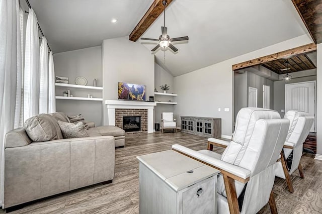 living room featuring vaulted ceiling with beams, ceiling fan, light hardwood / wood-style flooring, and a brick fireplace