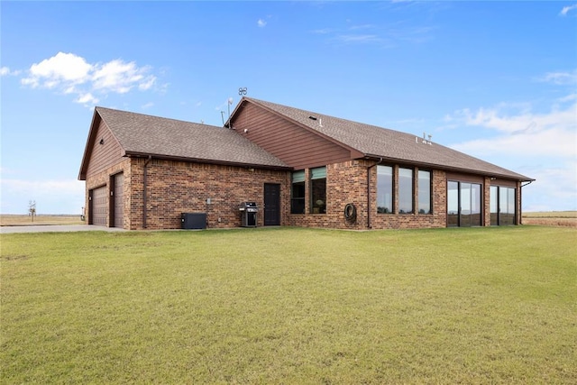 rear view of house with cooling unit, a garage, and a lawn