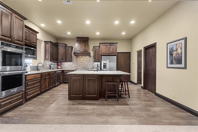 kitchen with a kitchen island, appliances with stainless steel finishes, a breakfast bar area, backsplash, and custom range hood