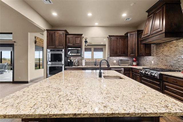 kitchen featuring appliances with stainless steel finishes, sink, a large island with sink, custom exhaust hood, and light stone counters