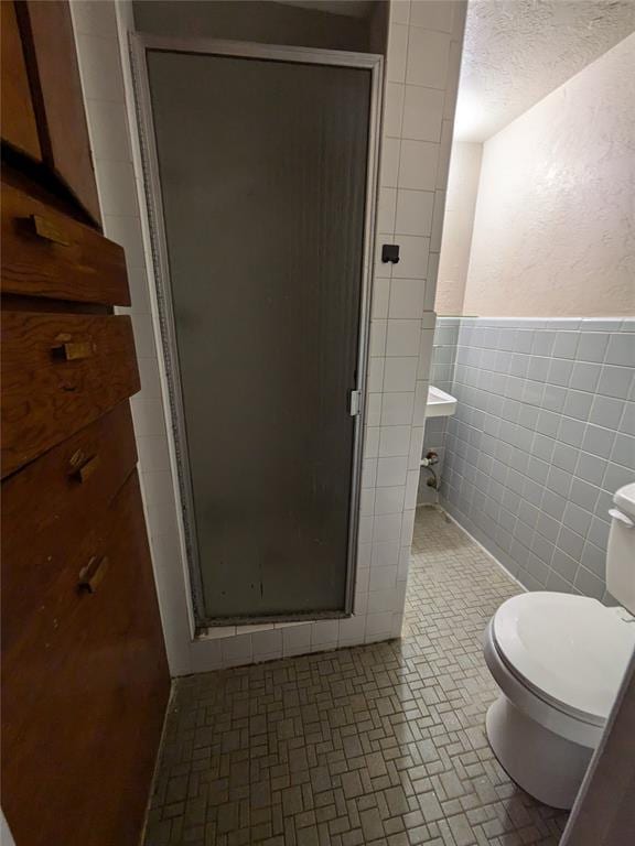 bathroom featuring a textured ceiling, a shower with shower door, tile walls, and toilet