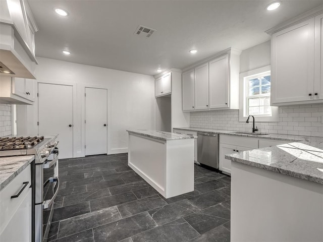 kitchen with sink, light stone countertops, appliances with stainless steel finishes, a kitchen island, and white cabinetry