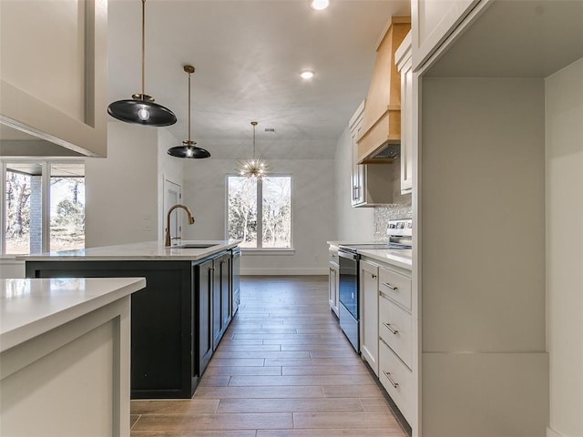 kitchen with pendant lighting, electric stove, sink, an island with sink, and white cabinetry