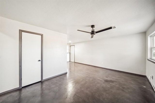 unfurnished room featuring finished concrete flooring, a ceiling fan, and baseboards