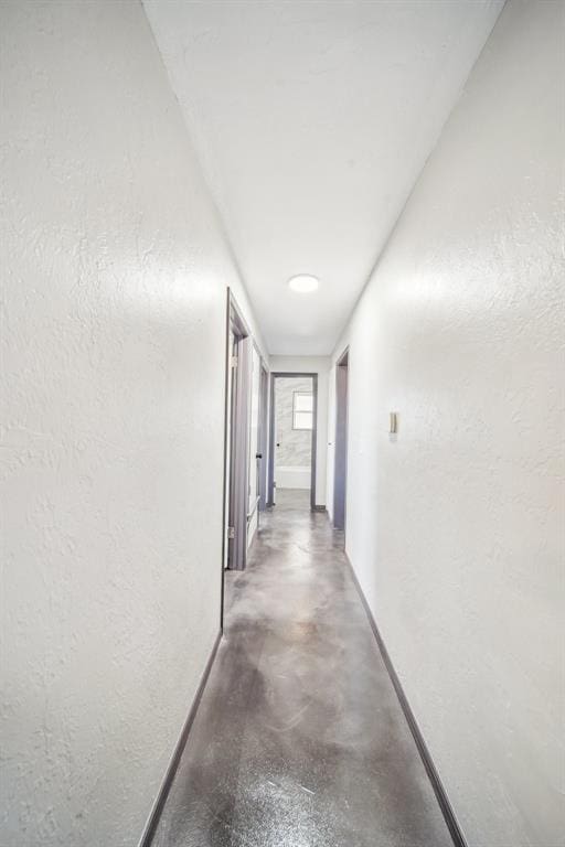 corridor with a textured wall, finished concrete flooring, and baseboards