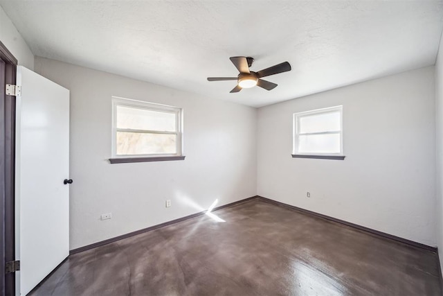 empty room featuring a ceiling fan, finished concrete floors, baseboards, and a wealth of natural light