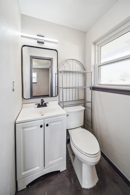 half bathroom featuring concrete flooring, vanity, toilet, and baseboards