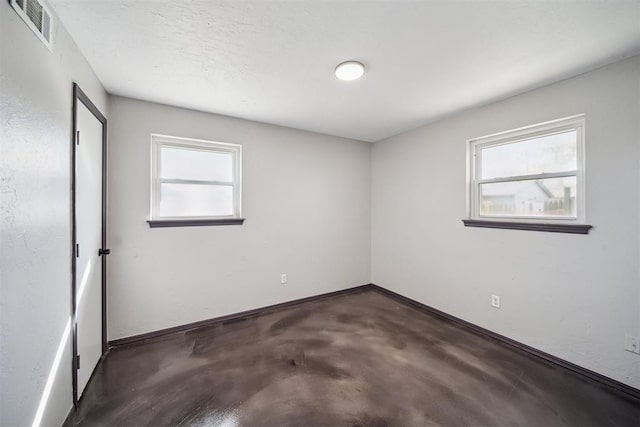 spare room featuring concrete flooring, visible vents, plenty of natural light, and baseboards