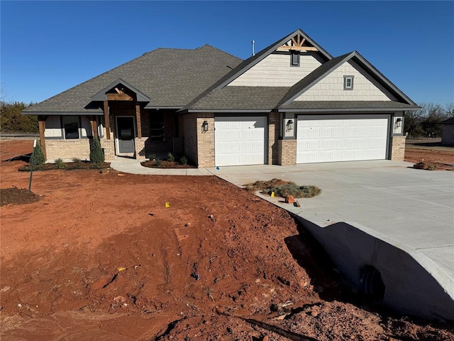 craftsman-style house featuring brick siding, driveway, an attached garage, and roof with shingles