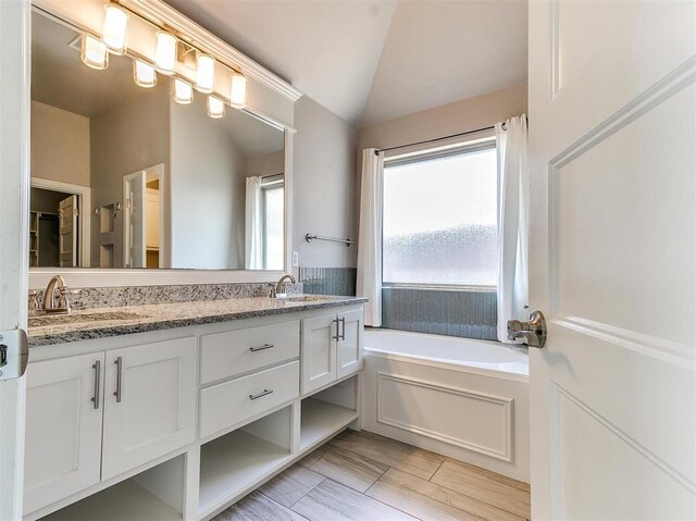 bathroom featuring a tub, hardwood / wood-style floors, vanity, and vaulted ceiling