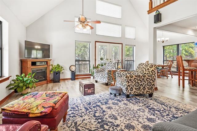 living room with french doors, light hardwood / wood-style flooring, high vaulted ceiling, and ceiling fan with notable chandelier