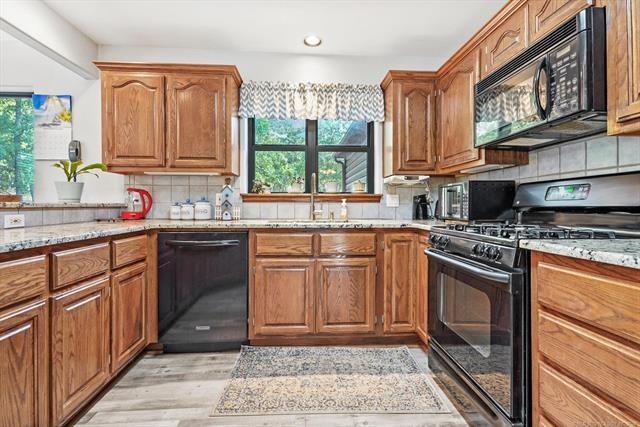 kitchen with a wealth of natural light, sink, black appliances, and light stone counters