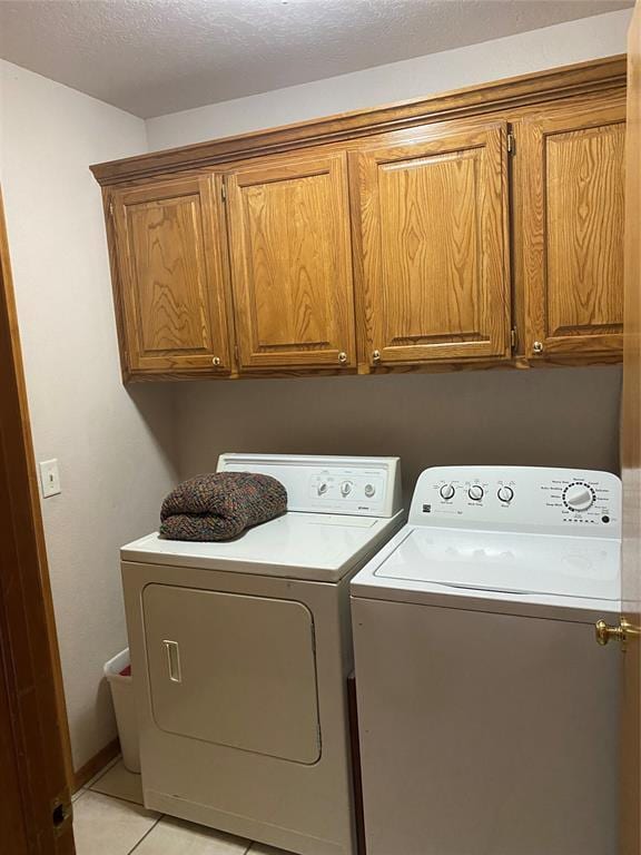 clothes washing area featuring independent washer and dryer, cabinets, a textured ceiling, and light tile patterned floors