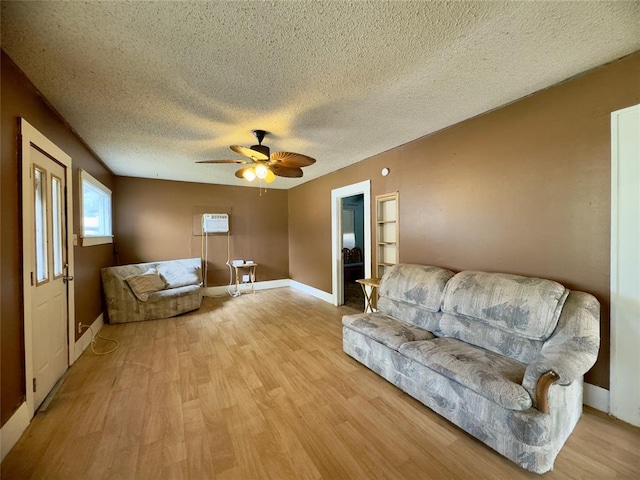 living room with a wall mounted air conditioner, a textured ceiling, light hardwood / wood-style floors, and ceiling fan