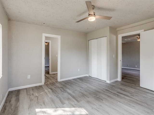 unfurnished bedroom with a textured ceiling, a closet, light hardwood / wood-style flooring, and ceiling fan