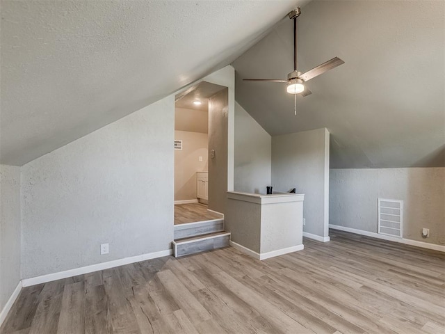 additional living space with a textured ceiling, ceiling fan, lofted ceiling, and light wood-type flooring