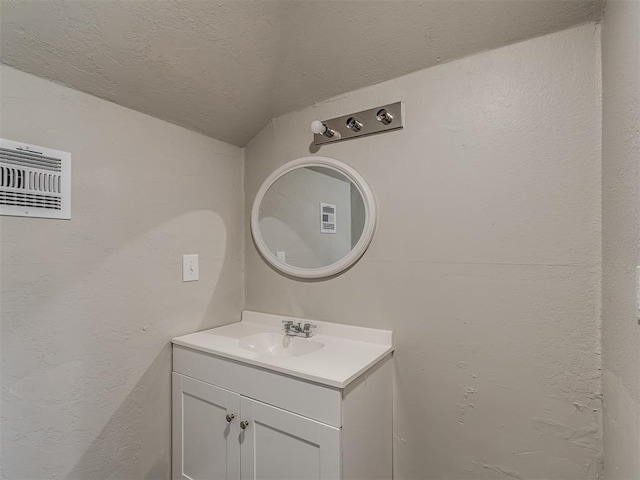 bathroom featuring vaulted ceiling, vanity, and a textured ceiling