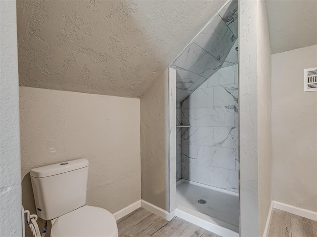 bathroom with hardwood / wood-style flooring, toilet, tiled shower, and vaulted ceiling