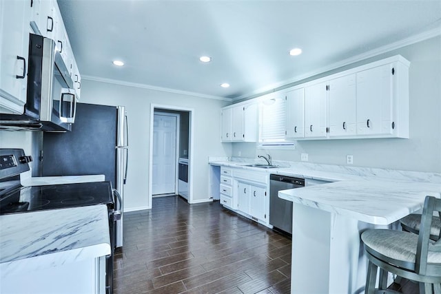 kitchen featuring appliances with stainless steel finishes, dark wood-type flooring, sink, white cabinets, and a breakfast bar area