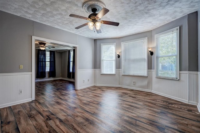 empty room with a textured ceiling, ceiling fan, plenty of natural light, and dark hardwood / wood-style floors