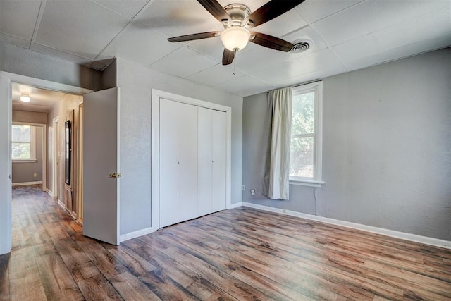 unfurnished bedroom with multiple windows, ceiling fan, a closet, and hardwood / wood-style flooring