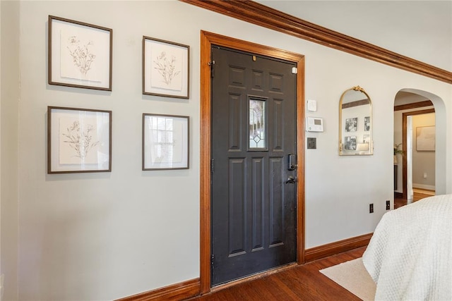 entryway featuring baseboards, arched walkways, dark wood finished floors, and crown molding