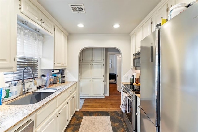 kitchen with sink, white cabinets, backsplash, light stone counters, and stainless steel appliances