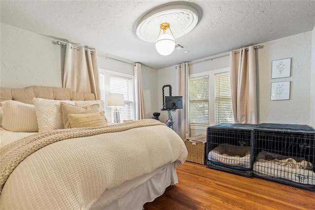 bedroom with multiple windows, a textured wall, a textured ceiling, and wood finished floors