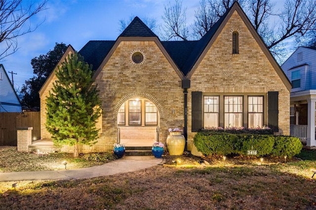 tudor-style house featuring brick siding and fence