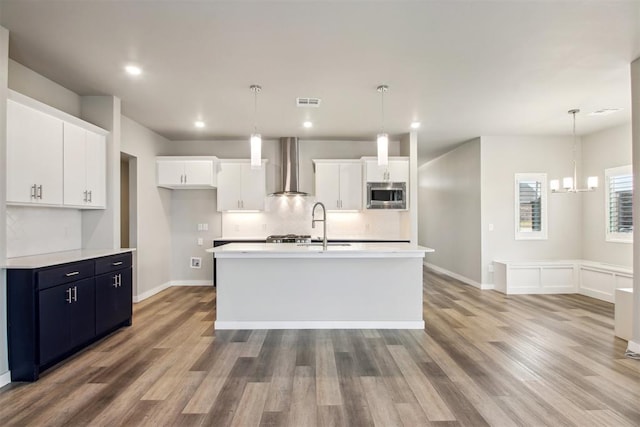 2200 El Cajon St, Edmond, OK 73034 - kitchen featuring wall chimney exhaust hood, stainless steel microwave, light countertops, white cabinetry, and light wood-style flooring
