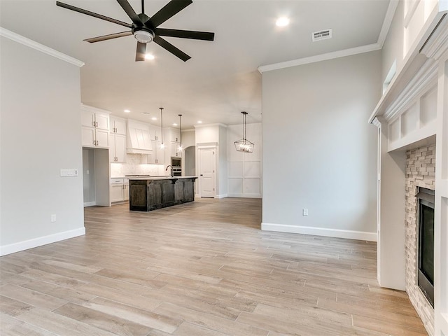 unfurnished living room with light wood-type flooring, ceiling fan, crown molding, and sink