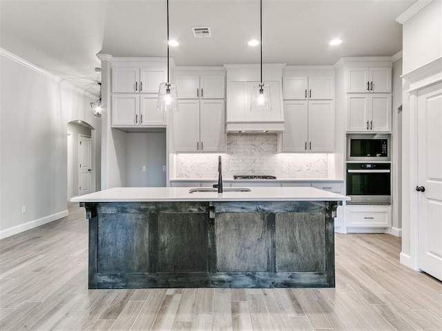 kitchen featuring white cabinets, pendant lighting, a center island with sink, and oven