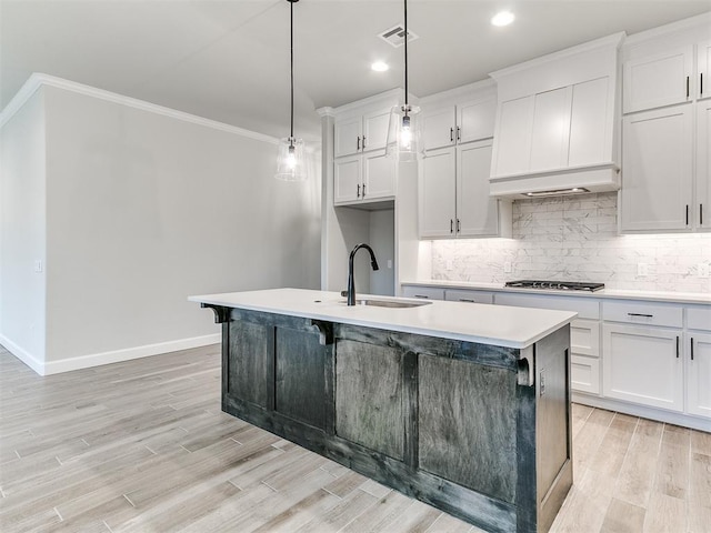 kitchen featuring ornamental molding, sink, white cabinets, hanging light fixtures, and an island with sink