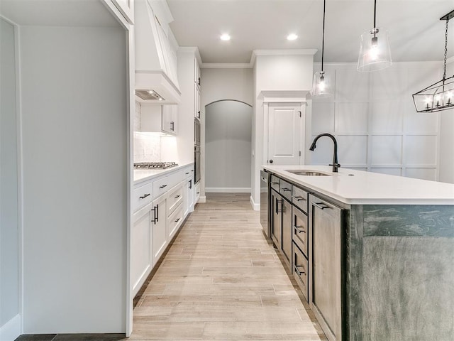 kitchen with premium range hood, a kitchen island with sink, sink, pendant lighting, and white cabinetry