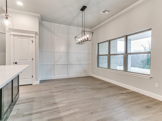 unfurnished dining area featuring light hardwood / wood-style floors, ornamental molding, and a notable chandelier