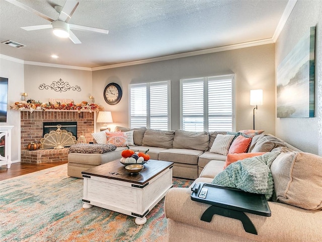 living room with hardwood / wood-style flooring, ornamental molding, ceiling fan, a brick fireplace, and a textured ceiling