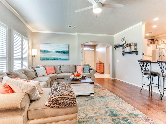 living room with hardwood / wood-style flooring, ornamental molding, ceiling fan, and a textured ceiling