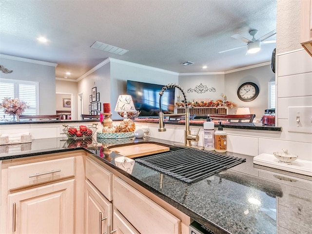 kitchen with sink, ceiling fan, ornamental molding, a textured ceiling, and dark stone counters