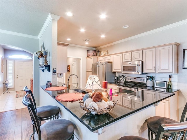 kitchen featuring wood-type flooring, a kitchen bar, ornamental molding, kitchen peninsula, and stainless steel appliances