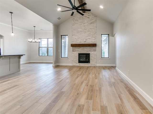 unfurnished living room with ornamental molding, ceiling fan with notable chandelier, light hardwood / wood-style flooring, high vaulted ceiling, and a stone fireplace