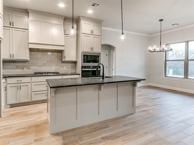 kitchen with sink, hanging light fixtures, a kitchen island with sink, appliances with stainless steel finishes, and ornamental molding