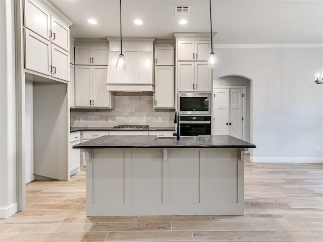 kitchen with a center island with sink, ornamental molding, decorative light fixtures, light hardwood / wood-style floors, and stainless steel appliances