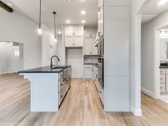 kitchen featuring a center island with sink, oven, white cabinets, sink, and hanging light fixtures