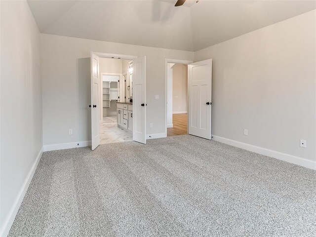 unfurnished bedroom with light carpet, a walk in closet, vaulted ceiling, and ceiling fan