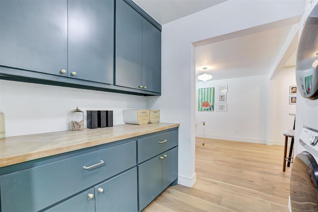 kitchen with blue cabinets, stacked washer and dryer, and light wood-type flooring