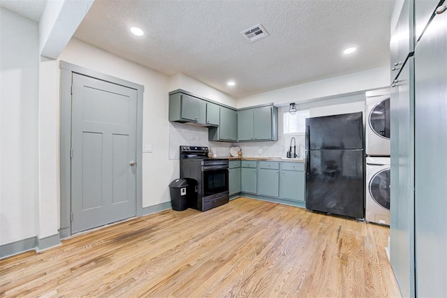 kitchen with electric stove, sink, stacked washing maching and dryer, black refrigerator, and light wood-type flooring