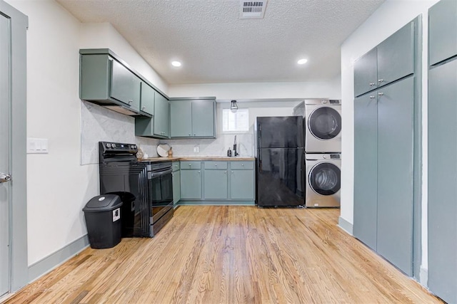 kitchen featuring stacked washer and dryer, light hardwood / wood-style flooring, tasteful backsplash, black appliances, and a textured ceiling