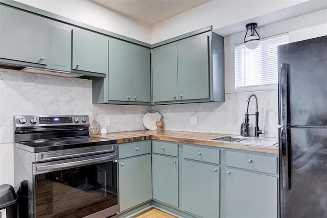 kitchen with sink, stainless steel range with electric stovetop, backsplash, butcher block counters, and black fridge